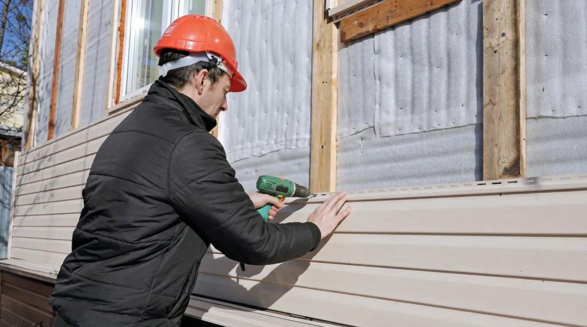 Siding replacement professional using a power drill to install new tan vinyl siding on a home exterior in Peoria, IL